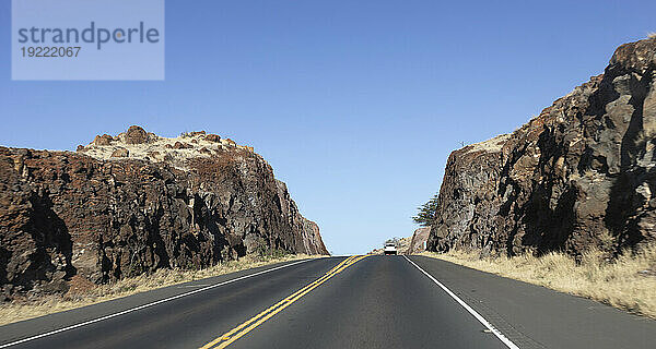 Auto fährt auf einer asphaltierten Autobahn durch die felsigen Klippen an einem Berghang mit blauem Himmel; Maui  Hawaii  Vereinigte Staaten von Amerika