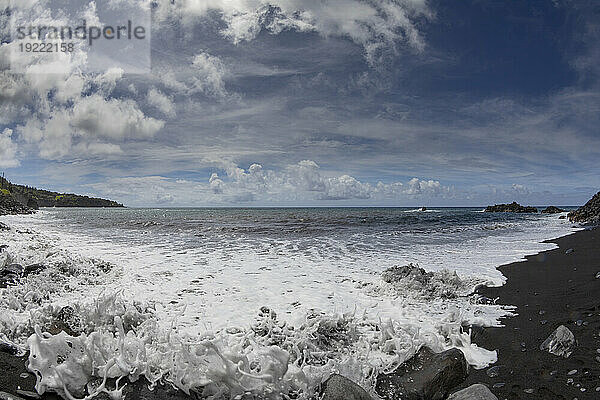 Malerische Aussicht auf den Pazifischen Ozean von einem schwarzen Lavasandstrand mit Meeresbrandung und blauem  bewölktem Himmel entlang der Straße nach Hana  malerische Route; Maui  Hawaii  Vereinigte Staaten von Amerika