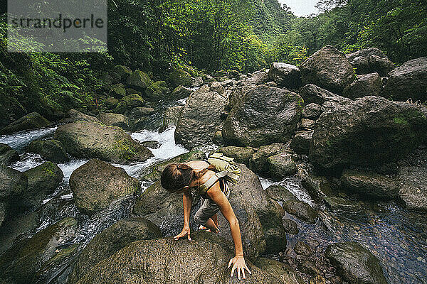 Blick von oben auf eine Frau  die über die rutschigen  nassen Felsen entlang des rauschenden Baches bei den Trafalgar Falls auf der Karibikinsel Dominica im Morne Trois Pitons Nationalpark klettert; Dominica  Karibik