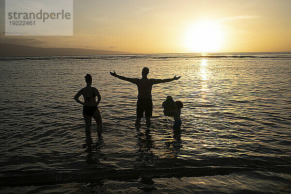 Blick von hinten auf die Silhouette einer Familie  die in der Dämmerung im Wasser steht und die Natur genießt; Baby Beach  Lahaina  Maui  Hawaii  Vereinigte Staaten von Amerika