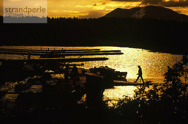 Silhouette einer Landschaft und eines Menschen auf einem Dock auf dem Weg zu einem Wasserflugzeug im Wood-Tikchik State Park  Alaska  USA; Alaska  Vereinigte Staaten von Amerika