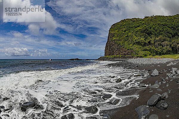 Malerische Aussicht auf den Pazifischen Ozean und baumbedeckte Klippen am Ufer eines schwarzen Lavasandstrandes mit Meeresbrandung und blauem  bewölktem Himmel entlang der Straße nach Hana  malerische Route; Maui  Hawaii  Vereinigte Staaten von Amerika