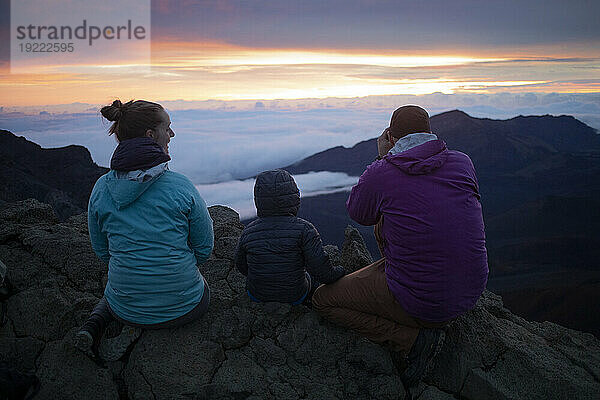 Familie auf einem Berggipfel über den Wolken bei Haleakala und beobachtet den Sonnenaufgang über der Pazifikküste; Haleakala-Nationalpark  Maui  Hawaii  Vereinigte Staaten von Amerika