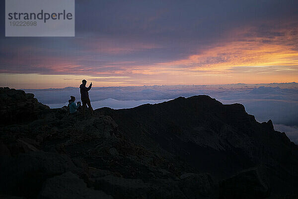 Familie auf einem Berggipfel über den Wolken bei Haleakala und beobachtet den Sonnenaufgang über der Pazifikküste; Haleakala-Nationalpark  Maui  Hawaii  Vereinigte Staaten von Amerika