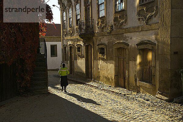 Von hinten beleuchtete Ansicht einer Frau  die eine gepflasterte Straße in einem Dorf entlang geht; Provesende  Flusstal des Douro  Portugal