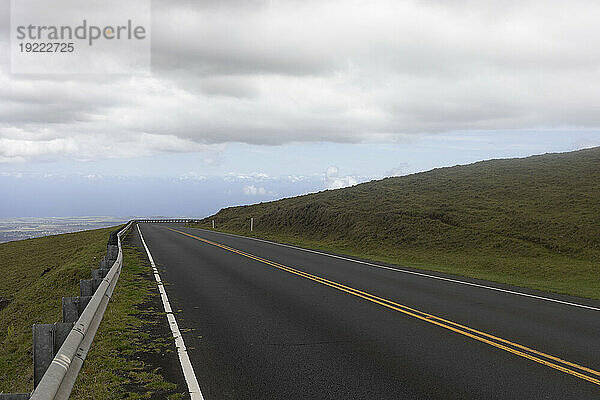 Gepflasterte Bergstraße mit grauer Wolkenbank über dem blauen Himmel entlang der malerischen Fahrt von Kihei nach Haleakala und zurück; Maui  Hawaii  Vereinigte Staaten von Amerika