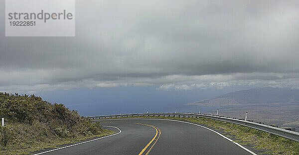 Kurvenreiche Bergstraße mit grauer Wolkenbank über dem blauen Himmel entlang der malerischen Fahrt von Kihei nach Haleakala und zurück; Maui  Hawaii  Vereinigte Staaten von Amerika