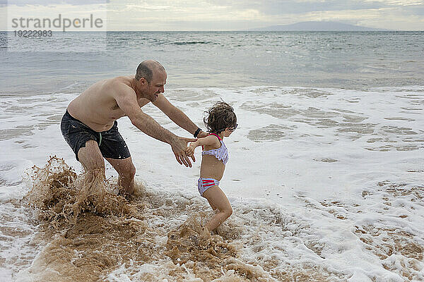 Nahaufnahme von Vater und Tochter  die in der schäumenden Brandung am Ufer des Kamaole Beach planschen und spielen; Maui  Hawaii  Vereinigte Staaten von Amerika