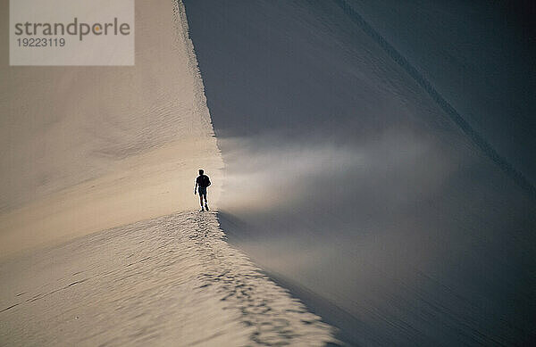 Eine Figur betritt den Weg des treibenden Sandes auf dem Kamm einer Düne  Tal des Mondes  Atacama-Wüste; Chile