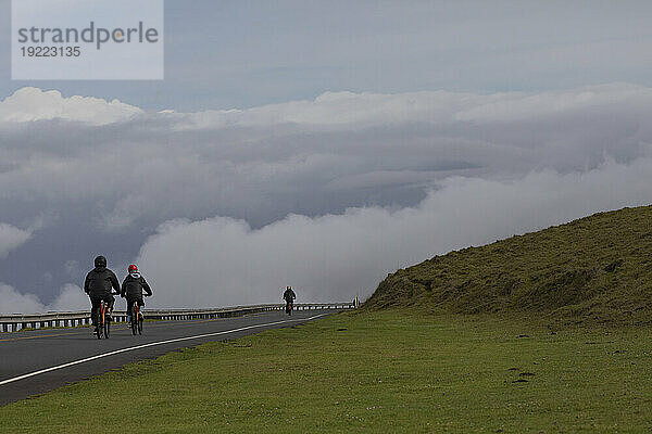 View taken from behind of people bicycling on the paved Road down from Haleakala  enjoying the dramatic views of of the clouds over the Pacific Coast; Maui  Hawaii  United States of America