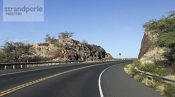 Gepflasterte Autobahn mit scharfer Kurve in der Straße durch die felsigen Klippen an einem Berghang mit blauem Himmel; Maui  Hawaii  Vereinigte Staaten von Amerika