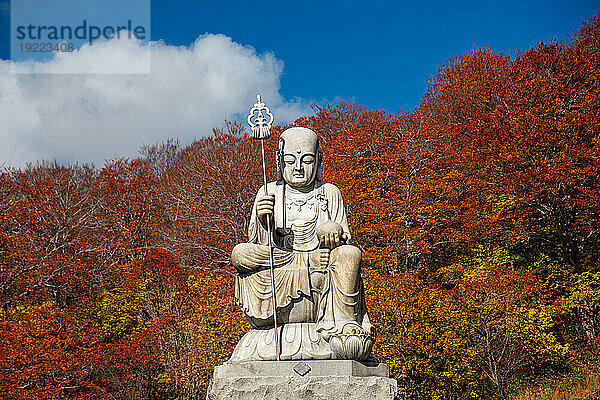 Große Shizo-Statue vor feuerroten Herbstblättern am wunderschönen japanischen Tempel  umgeben von Herbstfarben  Osorezan Bodaiji-Tempel  Mutsu  Präfektur Aomori  Honshu  Japan  Asien