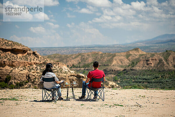 Ein Paar sitzt auf Stühlen mit einem Tisch und blickt auf eine wüstenartige Landschaft in der Nähe des Francisco Abellan-Staudamms  Granada  Andalusien  Spanien  Europa