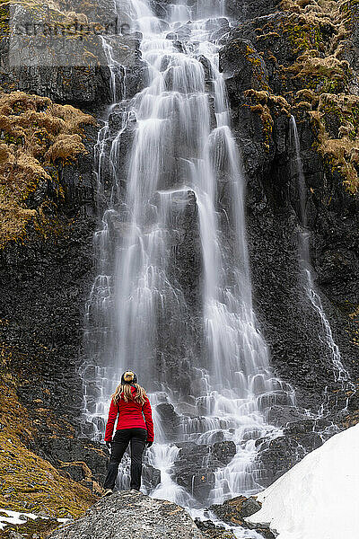 Blick von hinten auf eine Frau  die vor einem Wasserfall an der Strandir-Küste in der Nähe der Stadt Djupavik im Nordwesten Islands steht; Djupavik  Westfjorde  Island