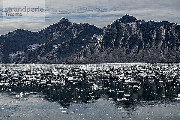 Zerklüftete Berggipfel umgeben das eisige  knurrende Wasser  das das ruhige Wasser im Nansen-Fjord bedeckt; Ostgrönland  Grönland