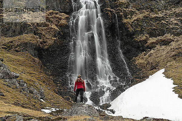 Blick von hinten auf eine Frau  die vor einem Wasserfall an der Strandir-Küste in der Nähe der Stadt Djupavik im Nordwesten Islands steht; Djupavik  Westfjorde  Island