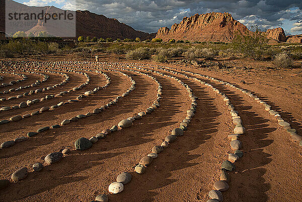 Wanderweg durch den Snow Canyon  mit Steinkreisen in einem Treffpunkt hinter dem Red Mountain Spa  mit Meditationslabyrinth und der Snow Canyon Mountain Range im Hintergrund. Red Cliffs Desert Reserve rund um St. George Town mit Felsklippen und dunklen Wolken am blauen Himmel; St. George  Utah  Vereinigte Staaten von Amerika