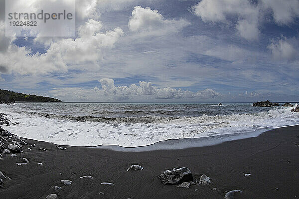 Malerische Aussicht auf den Pazifischen Ozean von einem schwarzen Lavasandstrand mit Meeresbrandung und blauem  bewölktem Himmel entlang der Straße nach Hana  malerische Route; Maui  Hawaii  Vereinigte Staaten von Amerika