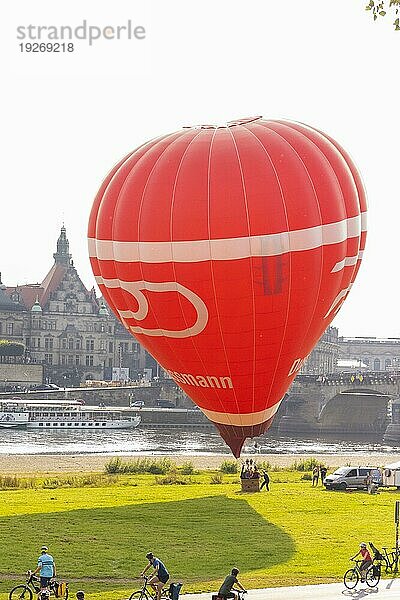 Ein roter Heißluftballon startet am Königsufer  gegenüber der historischen Silhouette der Dresdner Altstadt an der Elbe