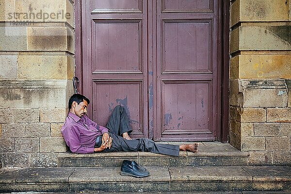 Ein Mann schläft an einem heißen Tag auf den Stufen eines Gebäudes in Colaba  Mumbai  Mumbai  Indien  Asien