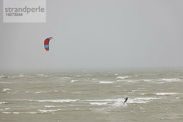 Einsamer Kitesurfer bei Sturm und schlechtem Wetter surft allein auf dem Meer  Portbail  Cotentin  Manche  Normandie  Frankreich  Europa