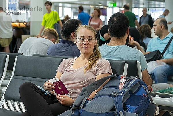 Wartehalle  Junge Frau wartet auf ihren Abflug mit Reisepass und Boardkarte  Check-In  Flughafen München  Bayern  Deutschland  Europa