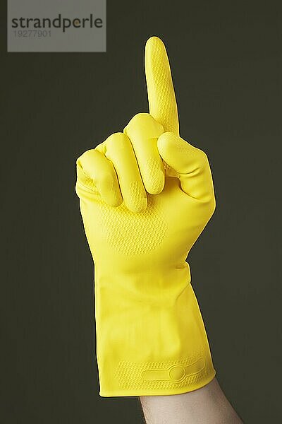 A Hand mit gelbem Gummischutzhandschuh  die mit dem Zeigefinger zeigt