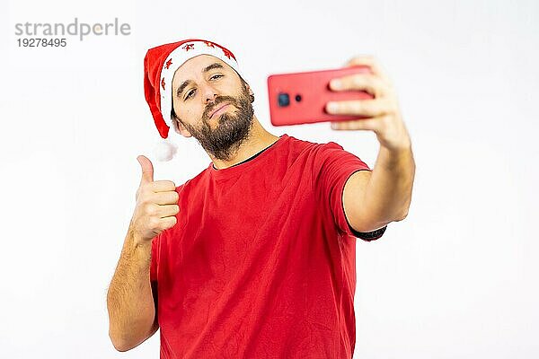 Sehr glücklicher junger kaukasischer Mann mit roter Weihnachtsmütze  der ein Selfie auf weißem Hintergrund macht  bekleidet mit einem roten TShirt Copy Paste