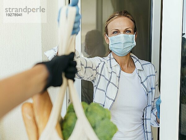 Frau mit medizinischer Maske zu Hause  die ihre Einkäufe selbständig abholt
