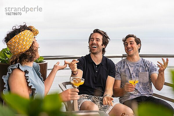 Freunde trinken Cocktails auf einem Dach mit Meerblick im Urlaub