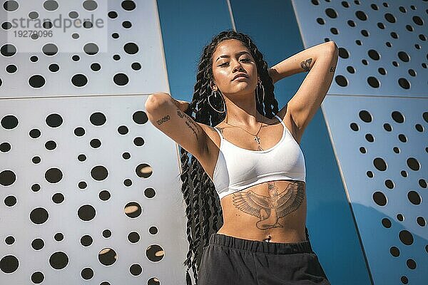 Junge Frau schwarzer Ethnie mit langen Zöpfen und Tattoos  in der Stadt  in die Kamera blickend