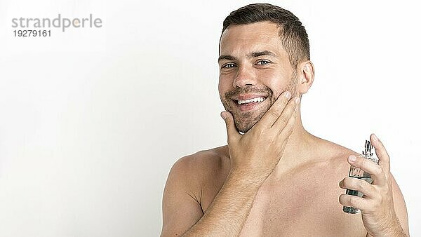 Glücklicher Mann sprüht Aftershave Lotion vor weißem Hintergrund