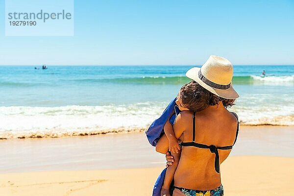 Mutter mit Hut  die ihren Sohn umarmt und sich mit ihm am Meer vergnügt  Algarve Strand  Albufeira. Portugal