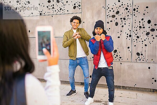 Urbaner Stil  zwei Jungs  die ein Video für soziale Netzwerke aufnehmen  zwei schwarze Latino Freunde  die Spaß auf der Straße haben. Afro Haar Junge  Brünette Junge mit langen Haaren mit Hut