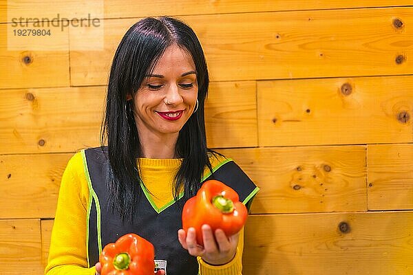 Ein brünettes kaukasisches Obstmädchen  das in einem Gemüseladen arbeitet  hat Spaß an roten Paprika in der Hand