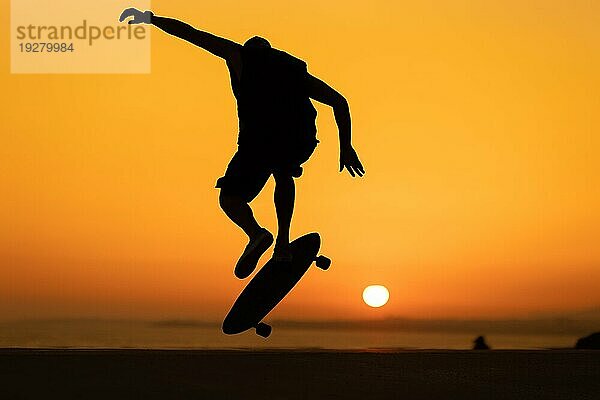 Silhouette eines Mannes  der bei einem orangefarbenen Sonnenuntergang einen Trick auf dem Skateboard vorführt. Mittlere Aufnahme