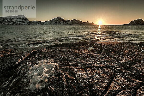 Der berühmte Sandstrand bei Haukland während des Sonnenuntergangs auf den Lofoten in Norwegen an einem klaren Wintertag mit schneebedeckten Bergen und blauem Himmel