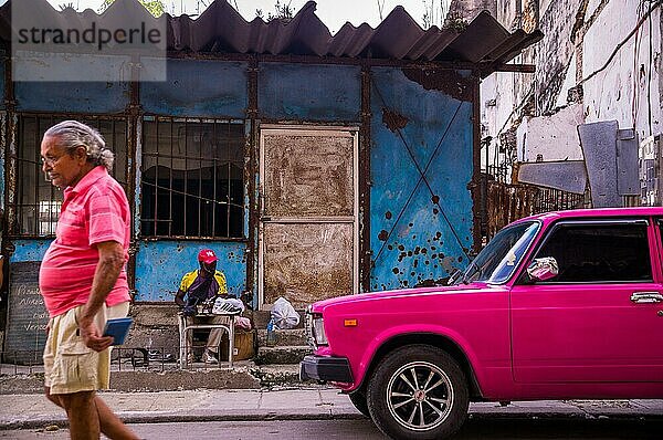 Havanna  Kuba am 23. Dezember 2015: Ein Mann geht eine Straße in Centro Habana entlang  sein Hemd hat die Farbe eines rosa Oldtimers