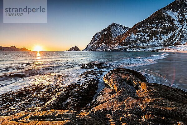 Der berühmte Sandstrand bei Haukland während des Sonnenuntergangs auf den Lofoten in Norwegen an einem klaren Wintertag mit schneebedeckten Bergen und blauem Himmel