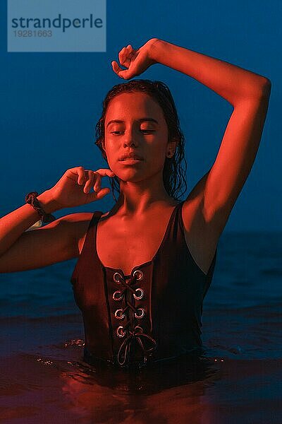 Lifestyle einer jungen hübschen brünetten Kaukasierin beim nächtlichen Baden im Meer mit einem beleuchteten roten Licht  der blauen Stunde in der Abenddämmerung
