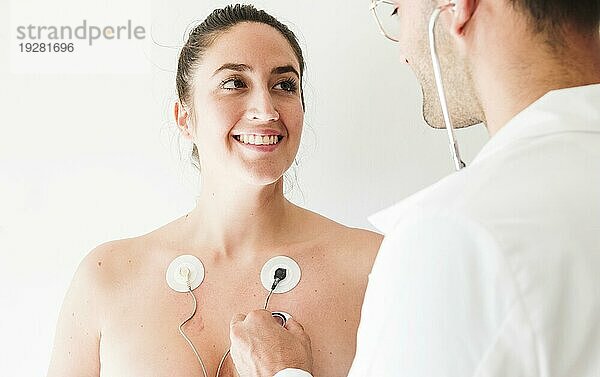 Arzt mit Stethoskop in der Nähe einer Frau mit Elektroden