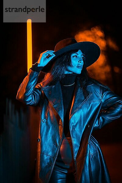 Mädchen mit Hut in einer Pose in der Nacht mit blauer led Beleuchtung. Winterabendmode