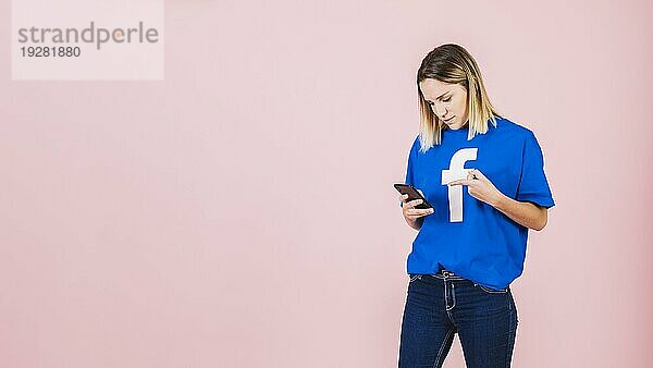 Junge Frau zeigt auf Mobiltelefon rosa Hintergrund