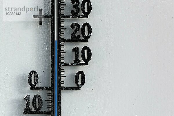 Klassisches schwarzes analoges Thermometer  das an einer weißen Wand hängt und eine blaue Temperaturskala von zwanzig  20 Grad Celsius anzeigt