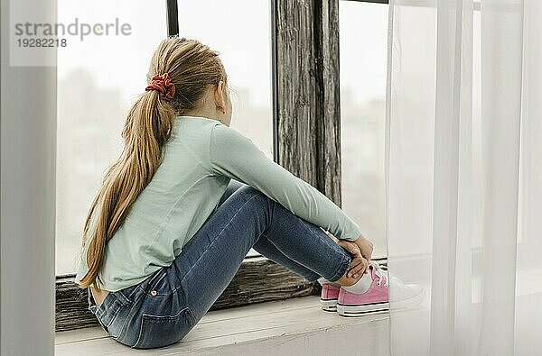 Seitenansicht kleines Mädchen sitzend Fensterbrett