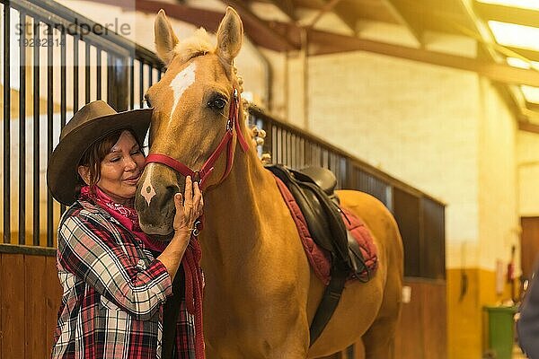 Porträt einer erwachsenen Frau in einem Pferdestall  die ein braunes Pferd streichelt  gekleidet in südamerikanische Tracht
