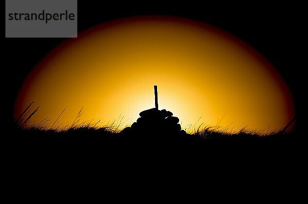 Silhouette eines Steinhaufens mit einem Stock bei Sonnenaufgang im Kreis