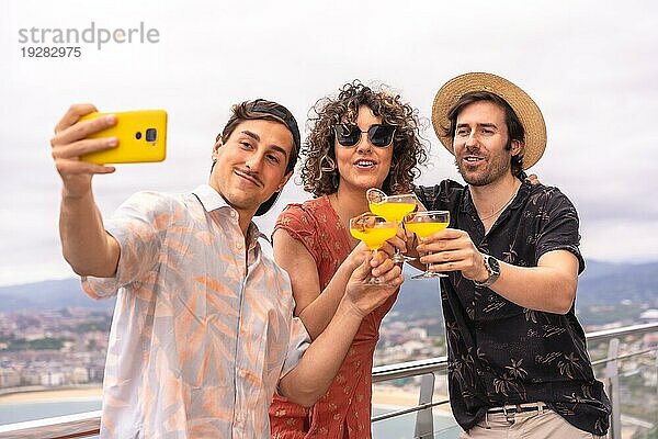 Drei Freunde stoßen an  während sie in den Ferien ein Selfie auf einer Terrasse machen