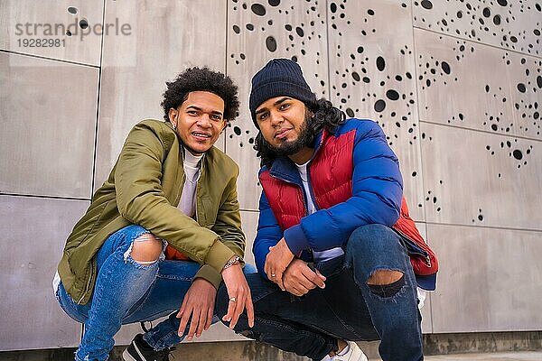 Urbaner Stil  Porträt von zwei schwarzen Latino Freunden  die Spaß auf der Straße haben. Afro Haar Junge  Brünette Junge mit langen Haaren mit Hut