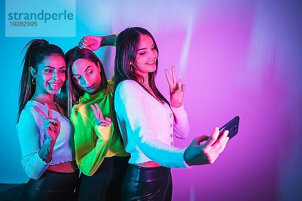 Lebensstil von Freunden  die in einer Disco mit blauen und rosa Neonlichtern feiern und ein Selfie mit dem Handy für soziale Netzwerke machen